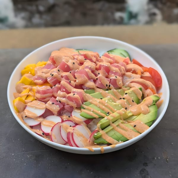 A vibrant poke bowl with tuna, avocado, mango, radishes, and tomatoes, drizzled with sauce.