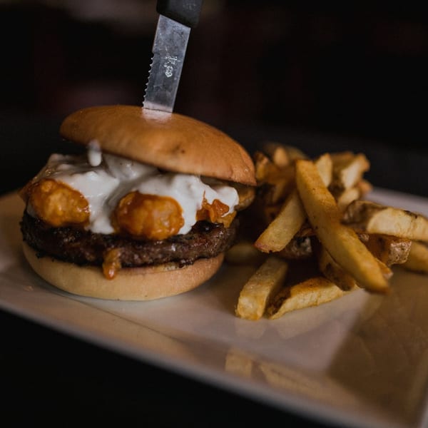 Doolittle's burger with white sauce and orange toppings, served with a side of fries.