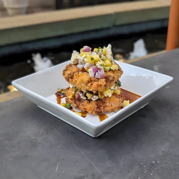 Two crispy fried cakes topped with corn, red onion, and white cheese, drizzled with sauce.