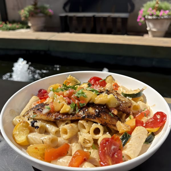 Doolittle's grilled fish pasta with tomatoes, zucchini, and pineapple salsa, next to a fountain.