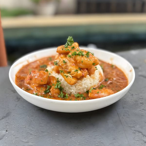 Doolittle's shrimp and grits, a white bowl filled with rice, shrimp, and red sauce.