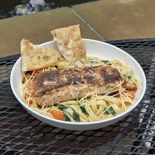 Doolittle's salmon pasta with cherry tomatoes, spinach, and garlic bread on a black mesh table.