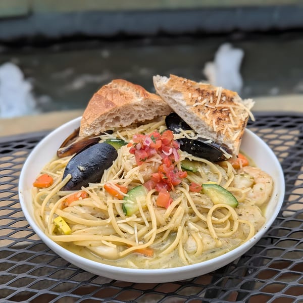 Doolittle's seafood pasta with mussels, shrimp, vegetables, and garlic bread on a patio table.